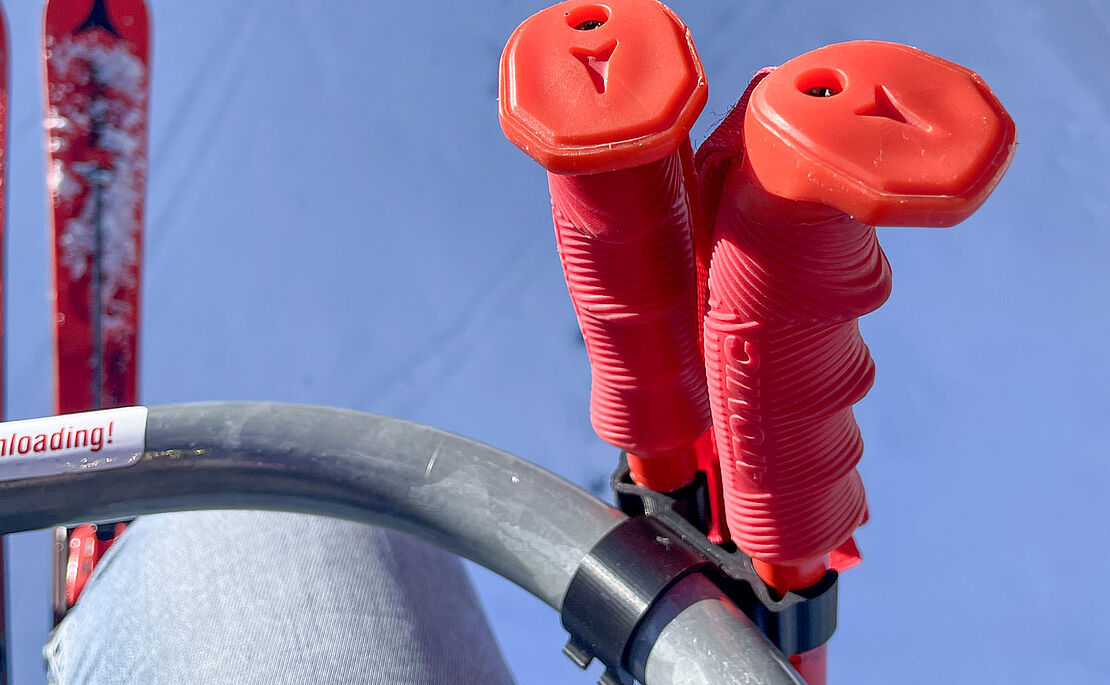 Ausschnitt eines Liftbügels, daran befestigt Skistöcke