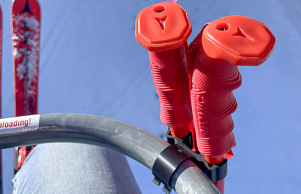 Ausschnitt eines Liftbügels, daran befestigt Skistöcke