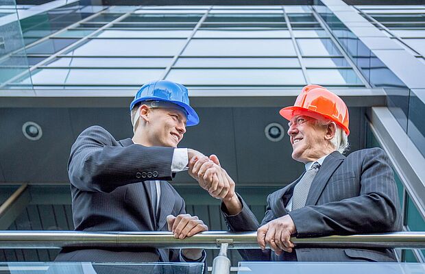 Zwei Männer auf der Baustelle mit Bauhelm am Kopf, die sich die Hände schütteln