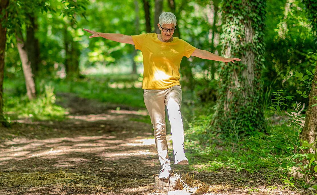 Frau, die einen Einbeinstand im Park auf einem Stein macht