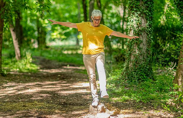 Frau, die einen Einbeinstand im Park auf einem Stein macht
