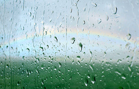 Regentropfen auf einer Scheibe aber im Hintergrund ein Regenbogen