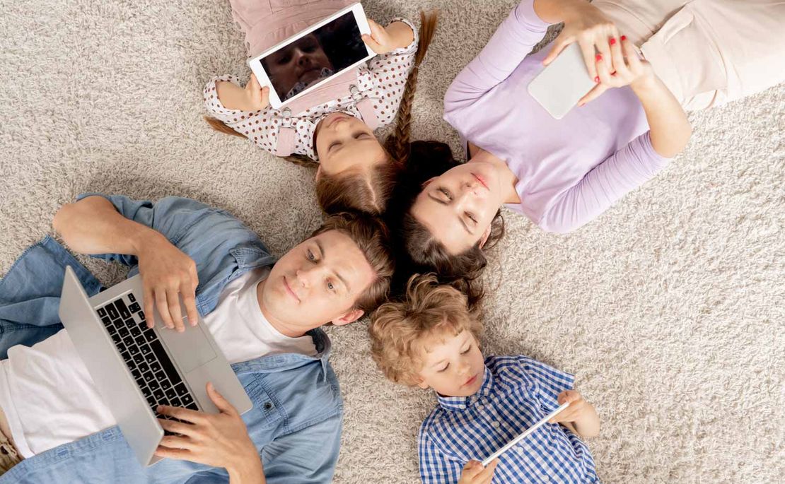 Familie liegt mit Laptop, Tablet, Handy & co. am Boden