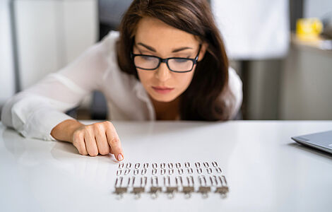 Braunhaarige Frau mit schwarzer Brille über Büroklammern gebeugt