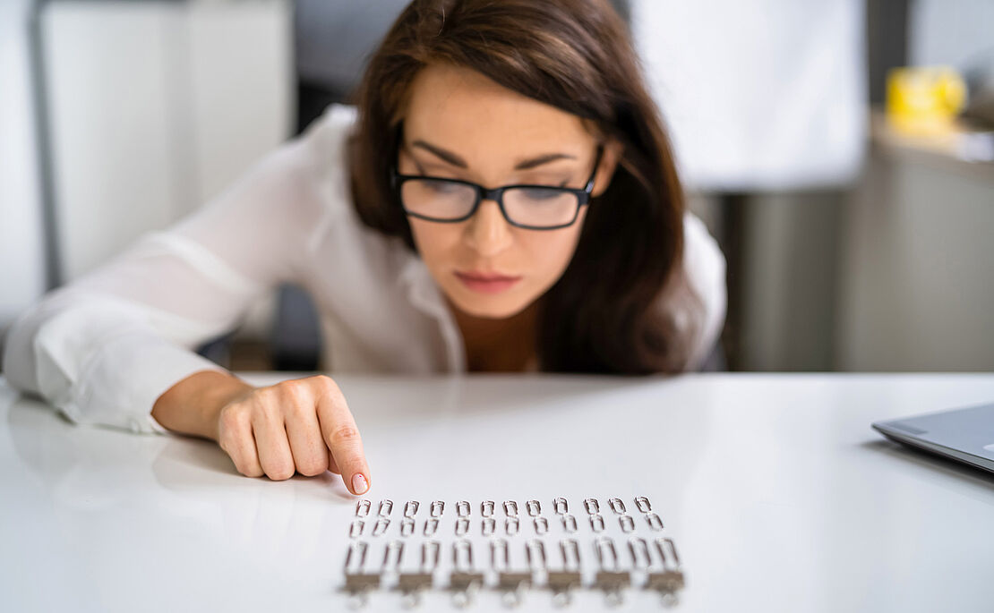 Braunhaarige Frau mit schwarzer Brille über Büroklammern gebeugt