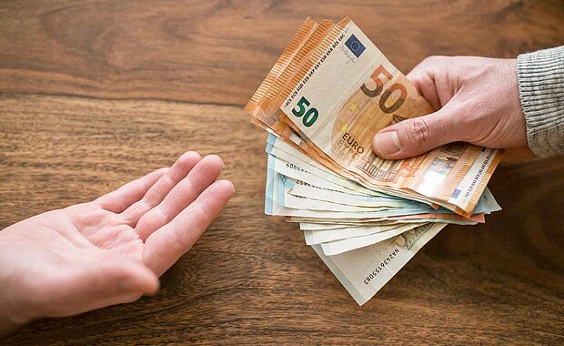 Eine offene Handfläche und eine zweite Hand, die Geldscheine zur ersten hält