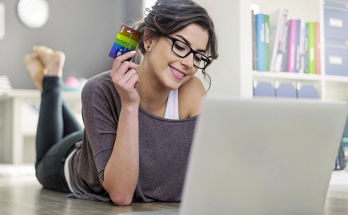 Frau lächelnd vor ihrem offenen Laptop liegend 