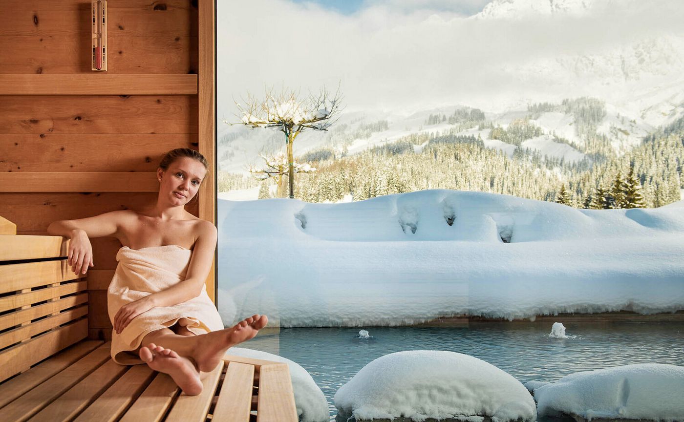 Frau in einer Sauna mit Blick auf Pool und verschneite Landschaft