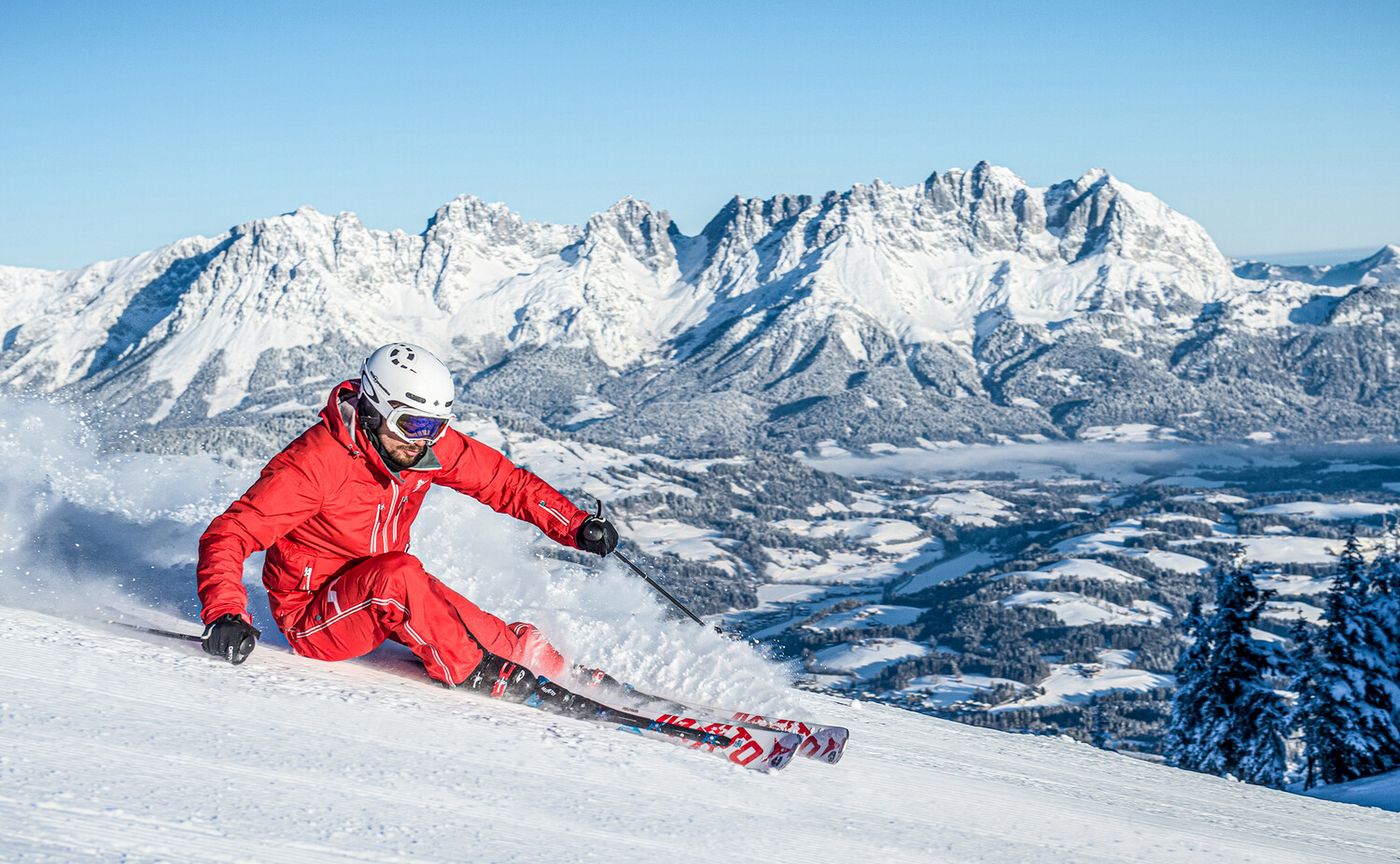 Skifahrer mit Sturzhelm und rotem Skioutfit auf Piste