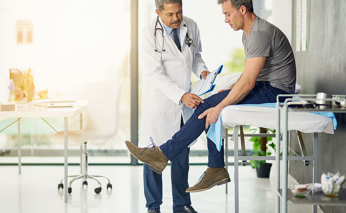 Mann sitzend auf einer Krankenliege, Arzt untersucht ihn