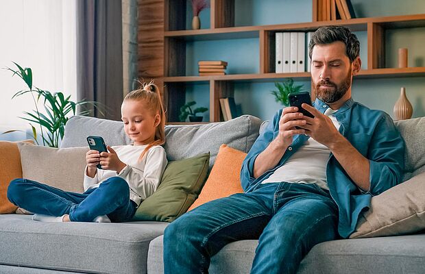 Vater und Tochter sitzen am Sofa mit Smartphone in der Hand
