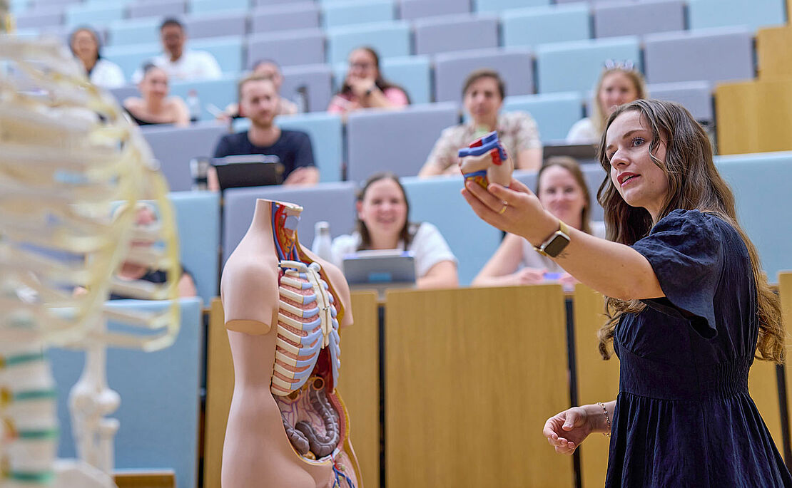 Vortragende im Hörsaal, die herausnehmbare Eingeweide aus einer Puppe präsentiert