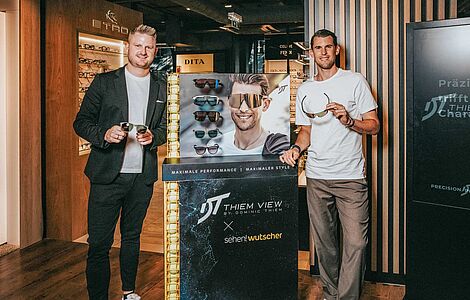Fritz Wutscher jr. und Dominic Thiem vor einem Brillengeschäft, jeder hält eine Sonnenbrille in der Hand, in ihrer Mitte ein Werbeständer