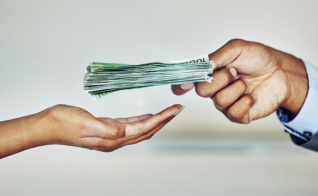 Geöffnete Frauenhand, in die eine Männerhand einen Packen 100-Euro-Scheine legt