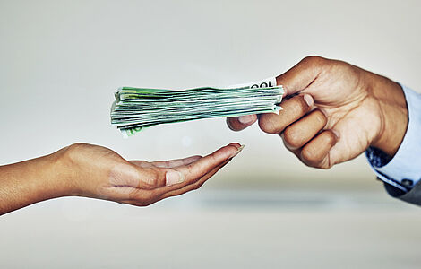 Geöffnete Frauenhand, in die eine Männerhand einen Packen 100-Euro-Scheine legt