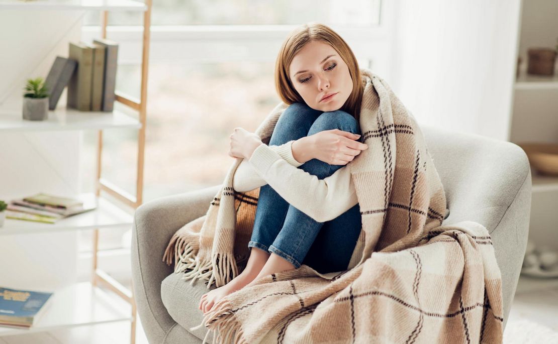 Depressive Frau am Sofa sitzend mit Decke