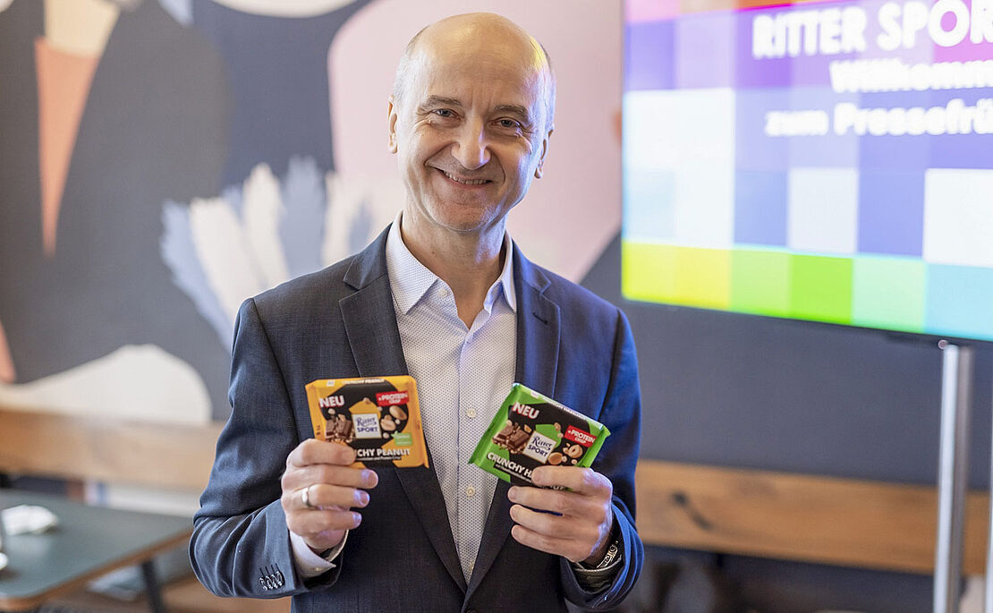 Foto von Wolfgang Stöhr mit den neuen Innovationen Vegan Tropical Coconut und Protein-Schokolade im 75-Gramm-Format