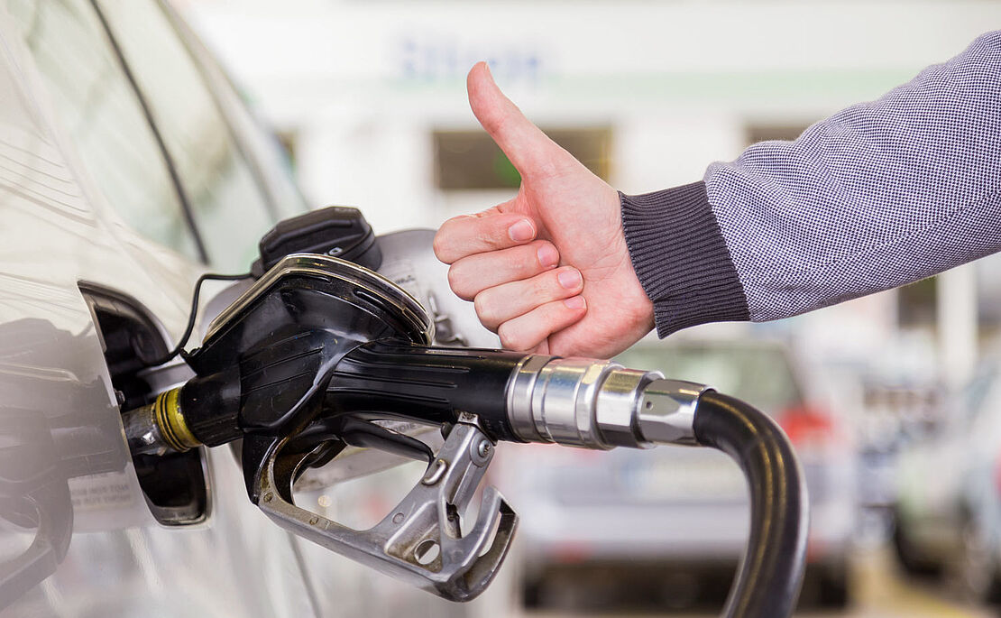Zapfpistole am Auto im Tank, davor eine Hand mit Daumen hoch