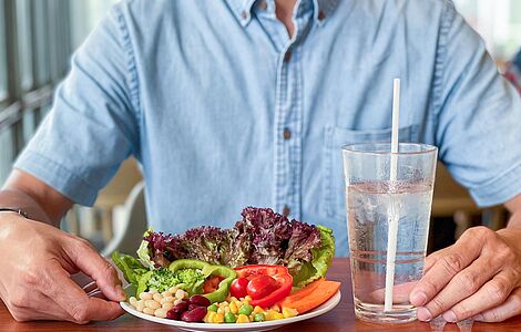 Mann sitzt vor einem Teller mit gesundem Gemüse und einem Glas Wasser