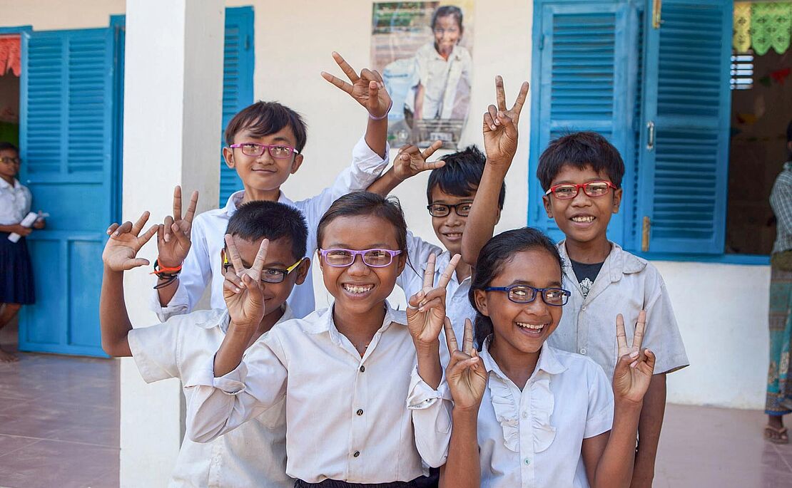 Gruppe von sechs Schulkindern, alle mit Brille, alle machen das Victoryzeichen