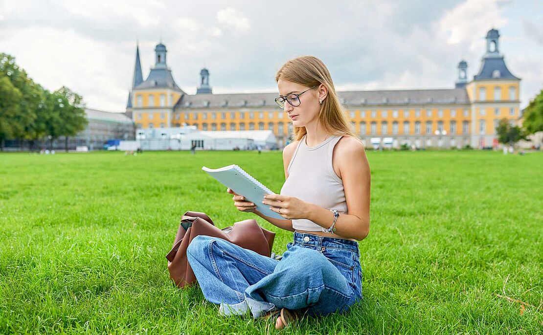 Mädchen, das einen Block liest und im Gras sitzt