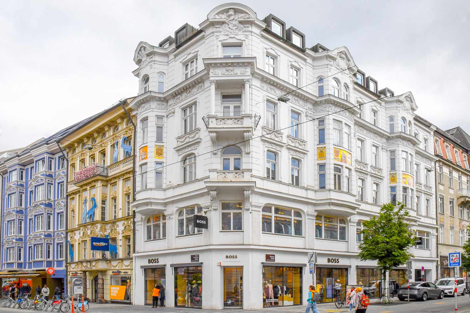 Weißes Eckhaus, links anschließend ein gelbes und blaues Zinshaus